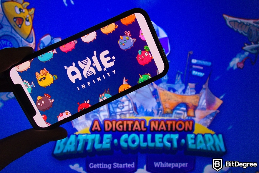 Best crypto games: a person holding a phone in front of an Axie Infinity poster.