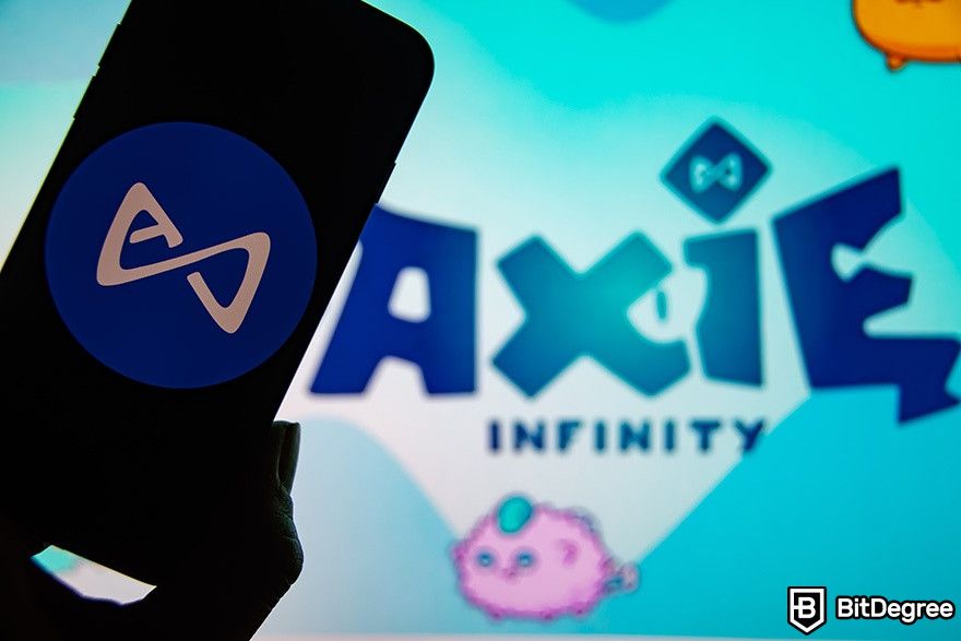 Best NFT games: Axie Infinity logo in the background, while a person is holding a phone in front of it.
