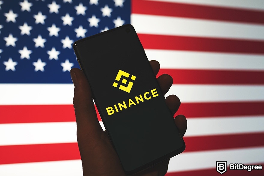 como usar a binance nos eua: celular com binance e bandeira dos eua ao fundo