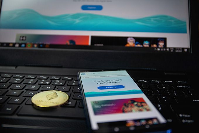 Sell NFT: OpenSea open on both a mobile device, and a laptop, with a physical Ethereum coin placed near them.