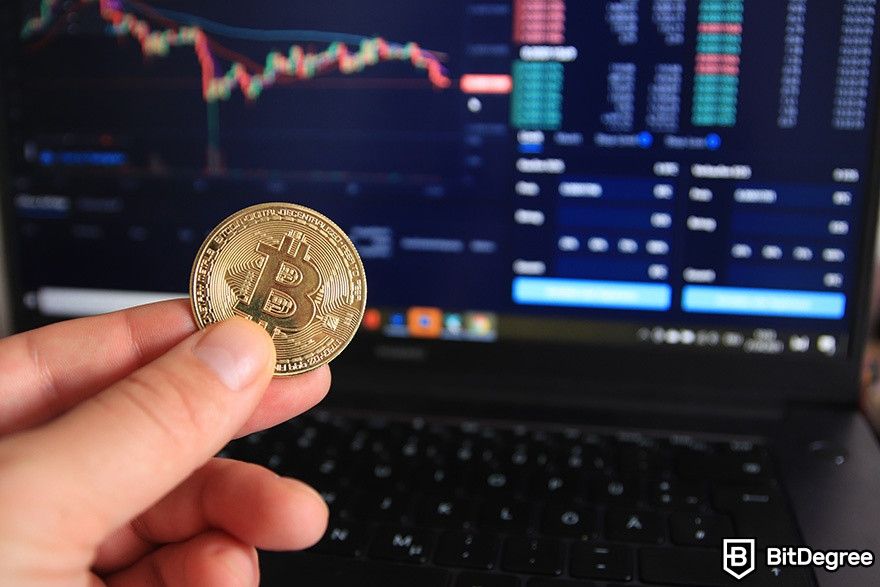 What is Curve Finance: a man holding a physical BTC coin in front of a laptop screen.