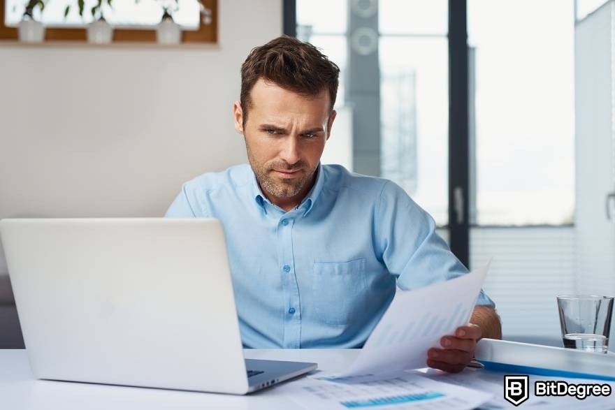 Best-paying jobs in finance: a man looking suspicious of financial sheets and charts on a laptop.