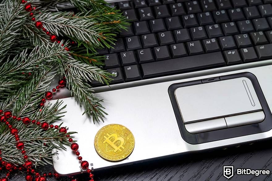 Buy gift cards with crypto: a physical Bitcoin is placed on a laptop next to a decorated fir branch.