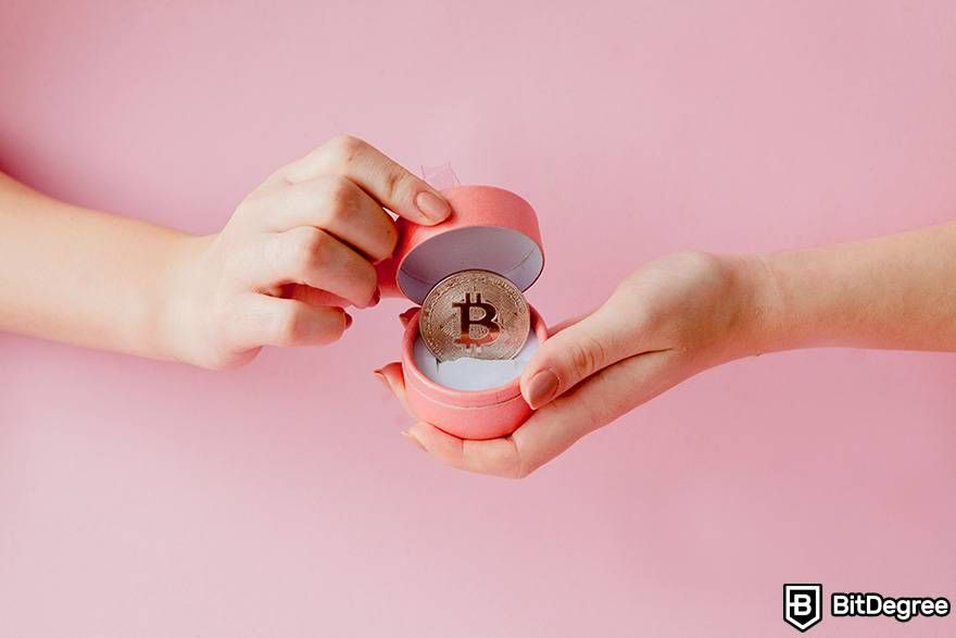 Buy gift cards with crypto: two hands are holding an opened ring box with a physical Bitcoin inside.