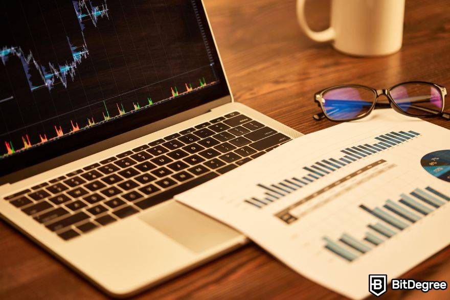 Strategi trading crypto terbaik: Grafik keuangan pada layar laptop dan kertas.