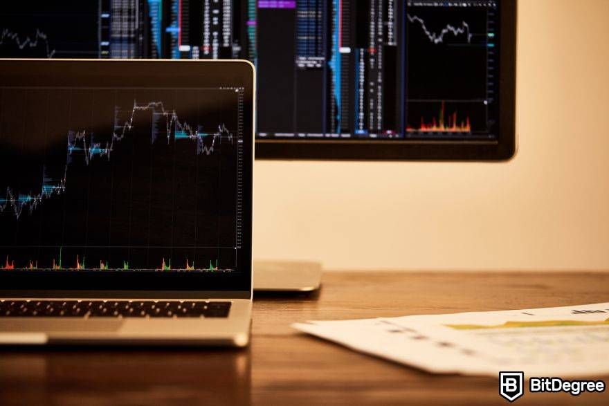 Crypto trading strategies: a laptop on a desk, in front of some financial charts.