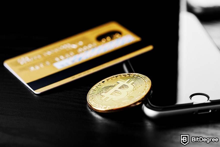 Cách mua tiền điện tử không KYC: một đồng Bitcoin vật lý được đặt bên cạnh thẻ ngân hàng và điện thoại thông minh.