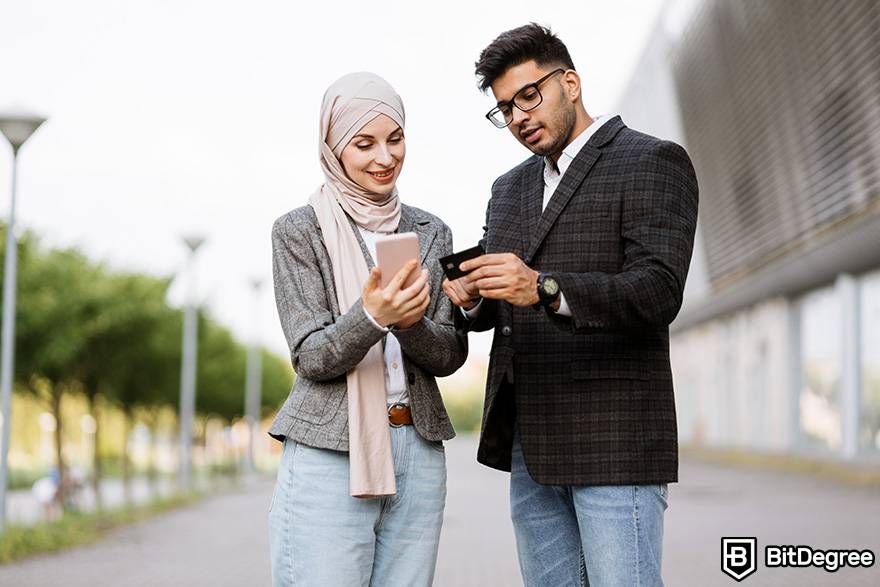 Cách mua tiền điện tử không KYC: một người phụ nữ và một người đàn ông đang nhìn vào điện thoại thông minh của họ và nói chuyện.