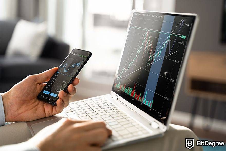 What is arbitrage trading in crypto: person holding laptop and phone to trade.