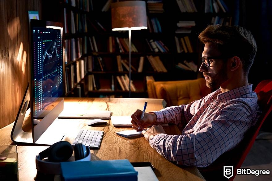 What is margin trading crypto: a man is looking at market charts on a monitor and taking notes.