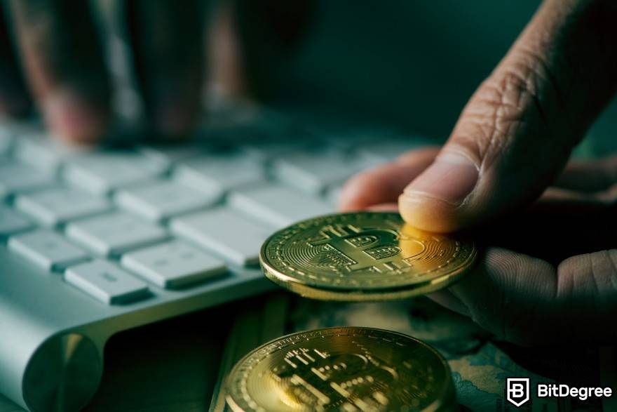 What is wash trading crypto: a person holding a physical BTC coin near a keyboard.