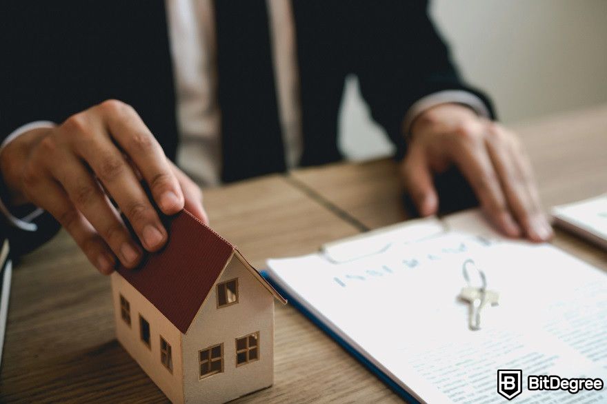 Benefits of cryptocurrency: A real estate agent about to give a document and house miniature.