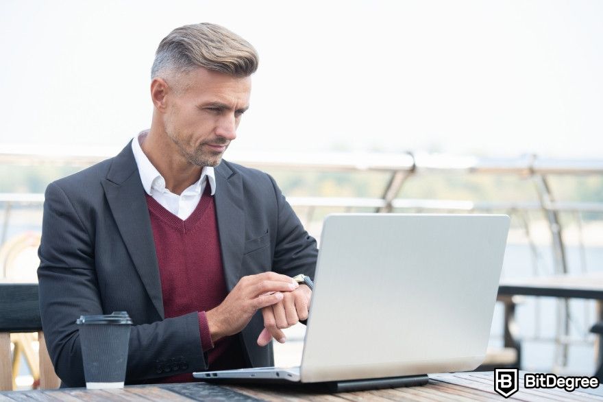 Best AI chatbot: A with a laptop checking the time on his watch.