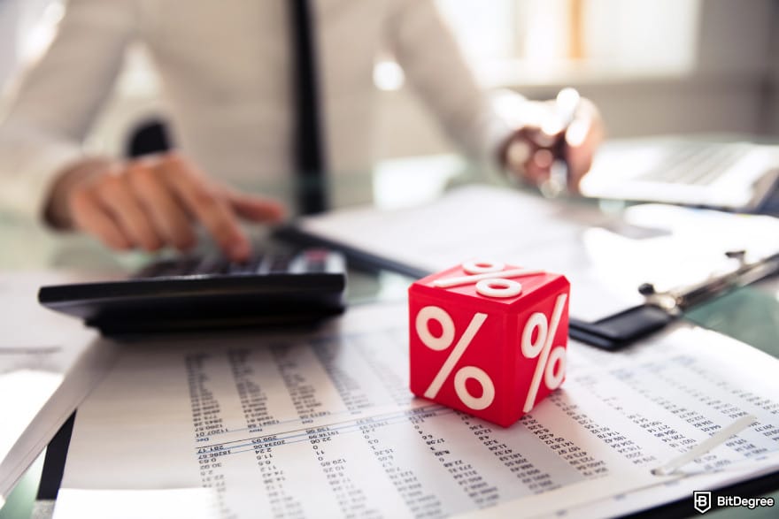 Best Bitcoin ETF UK: A close-up of a red cubic block showing a percentage sign with a man calculating in the background.