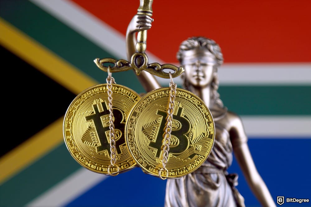 Best crypto exchange South Africa: the statue of Lady Justice holding scales with two Bitcoin coins hanging from them, against the backdrop of the South African flag.