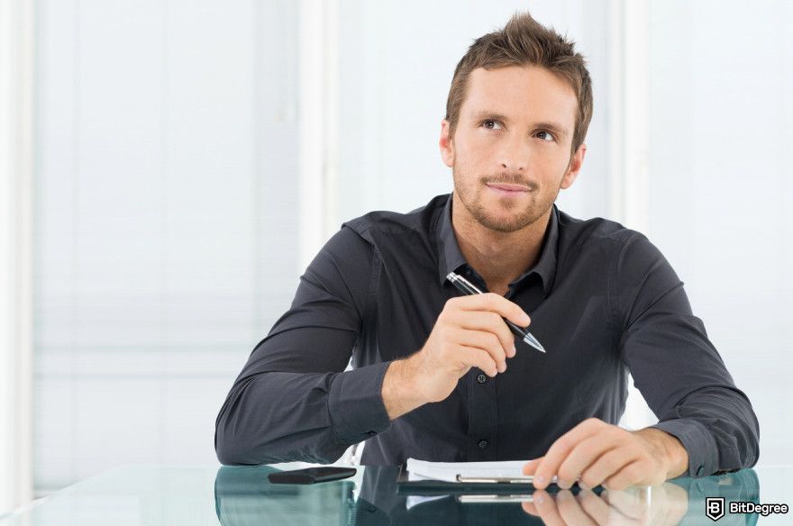 Best crypto futures trading platform: a man seated at a desk holding a pen.