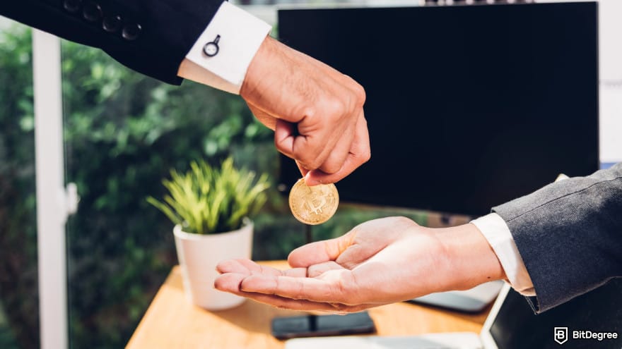 Best crypto liquidity providers: a person in a business suit handing a physical Bitcoin token to another person.