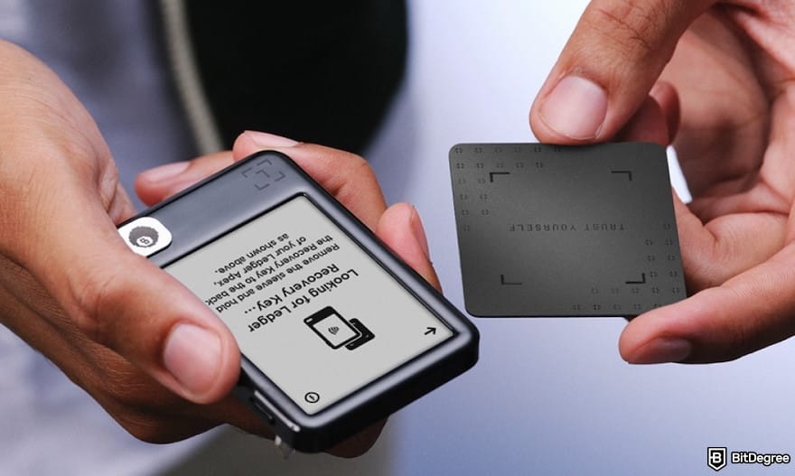 Best crypto wallet for business: a pair of hands holding Ledger Nano Gen 5 and a recovery key card.