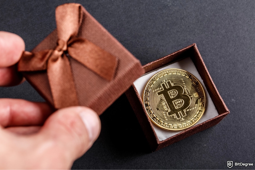 Best free crypto airdrops: a person opening a gift box with a Bitcoin inside.