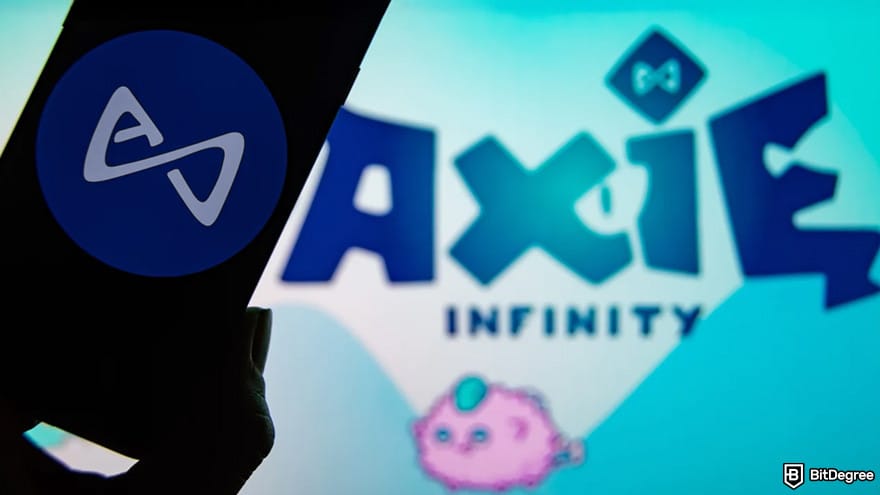 Best NFT games: Axie Infinity logo in the background, while a person is holding a phone in front of it.