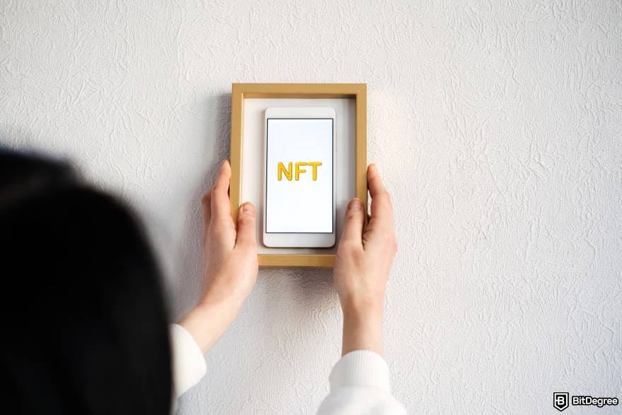 Best NFT wallet: a person holds up a smartphone displaying the letters "NFT" inside a wooden frame.