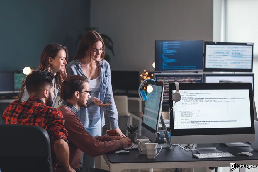 Best programming courses for beginners: a group of young people gathering in front of a computer displaying lines of codes.