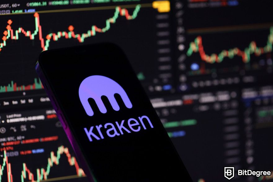 Stablecoin tốt nhất: điện thoại hiển thị logo sàn giao dịch Kraken ở phía trước màn hình hiển thị biểu đồ.