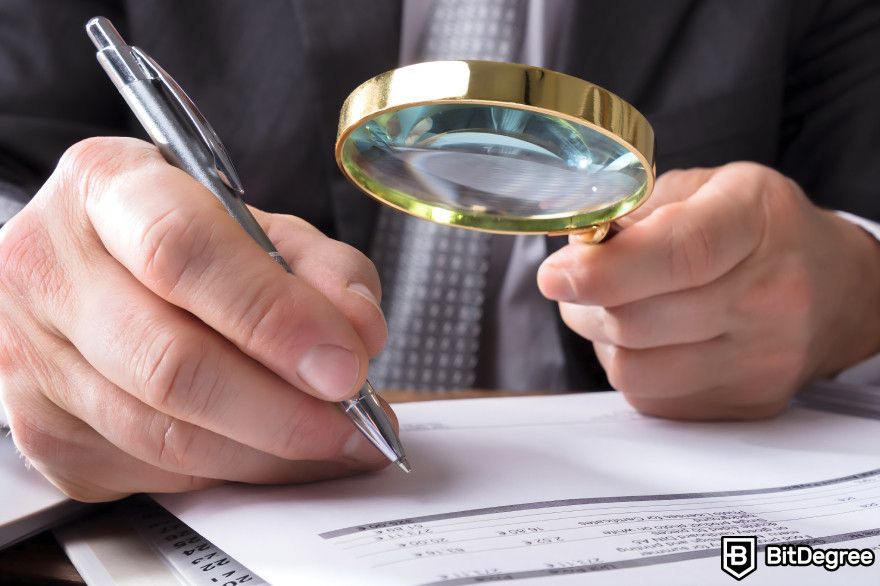 Best stablecoin: a close-up of a person's hand as it writes while also holding a magnifying glass.