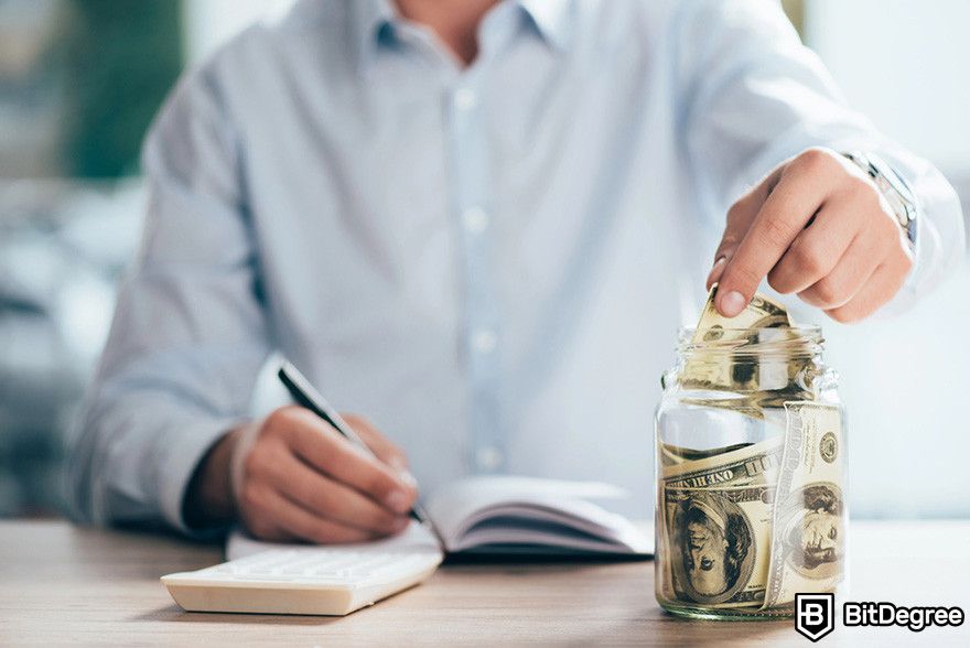 Blockchain accounting: a person writing on a notebook while putting a 100 dollar bill into a jar.