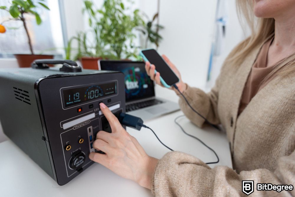 Blockchain for energy: a woman holding a smartphone charged on a portable power supply.