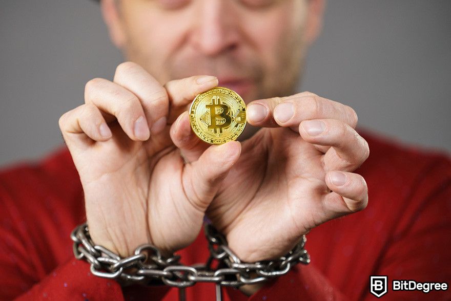 Blockchain in banking: a person holding a Bitcoin coin with his hands bound by chain.