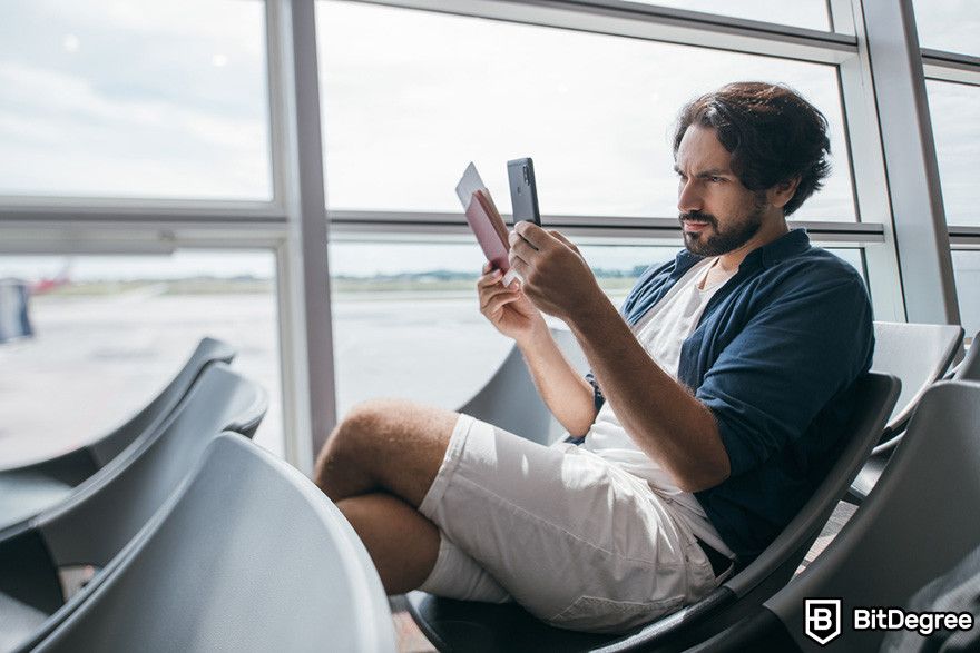 Blockchain em seguros: um homem em um terminal de aeroporto segurando um smartphone e um passaporte, olhando para a tela do celular.