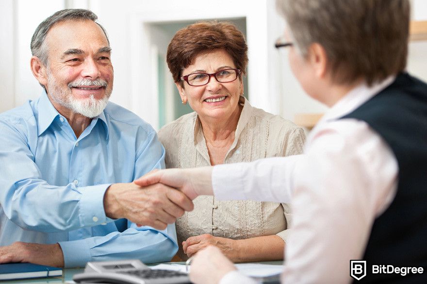 Blockchain in insurance: an elderly couple smiles while shaking hands with a business person across a desk.