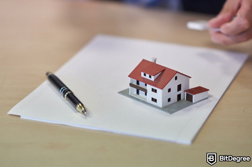 Blockchain in real estate: A miniature house sitting on top of a piece of paper with a pen beside it.