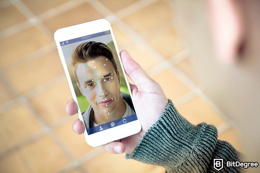 Blockchain marketing: Man holding smartphone displaying facial recognition.