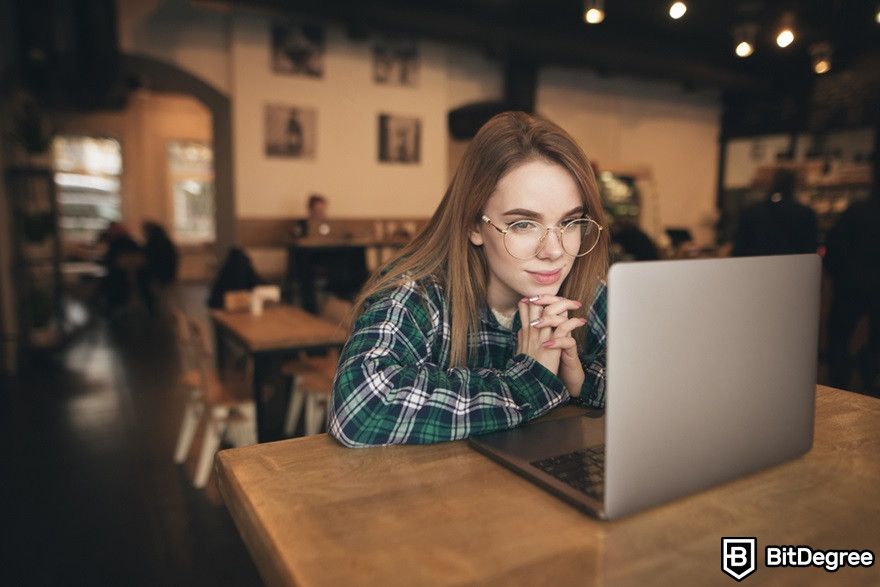 Marketing de blockchain: Uma mulher sentada em um café sorrindo enquanto olha para um laptop.