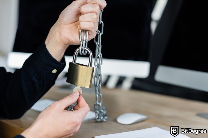 Blockchain security: Cropped view of programmer holding padlock and key near blurred computers.
