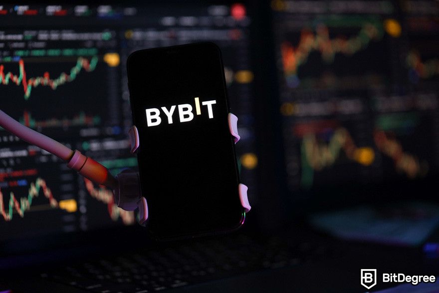 Bybit affiliate: Bybit cryptocurrency exchange displayed on a smartphone held against a backdrop of financial charts.