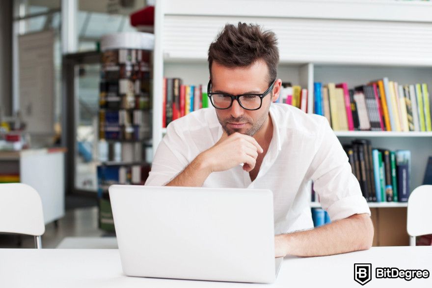 Cardano staking: a man wearing glasses is seated at a table focused on his laptop.