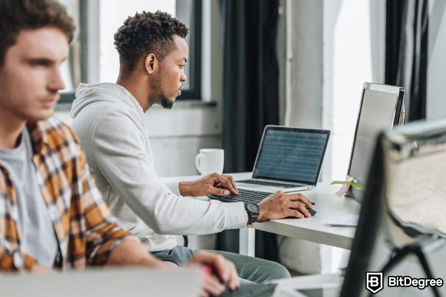 Cardano staking: two programmers working in front of computers in an office environment.