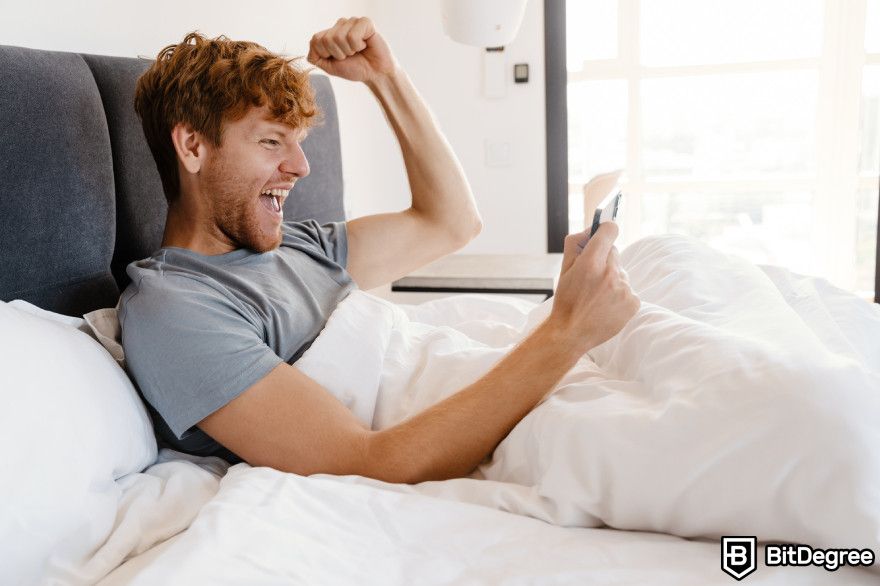 Polygon staking: a man sits in bed ecstatic while holding his phone.