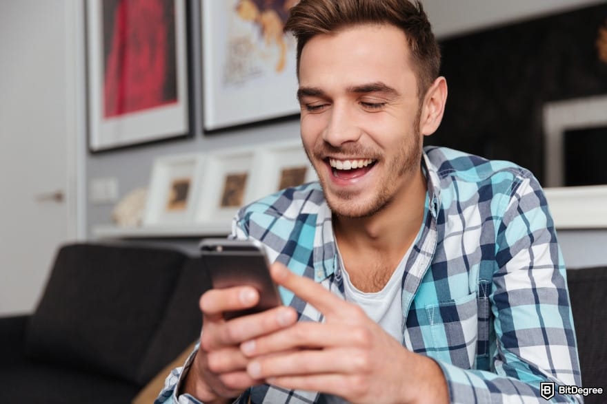Cheapest way to send money to Philippines: young laughing man sitting in home and looking at phone.