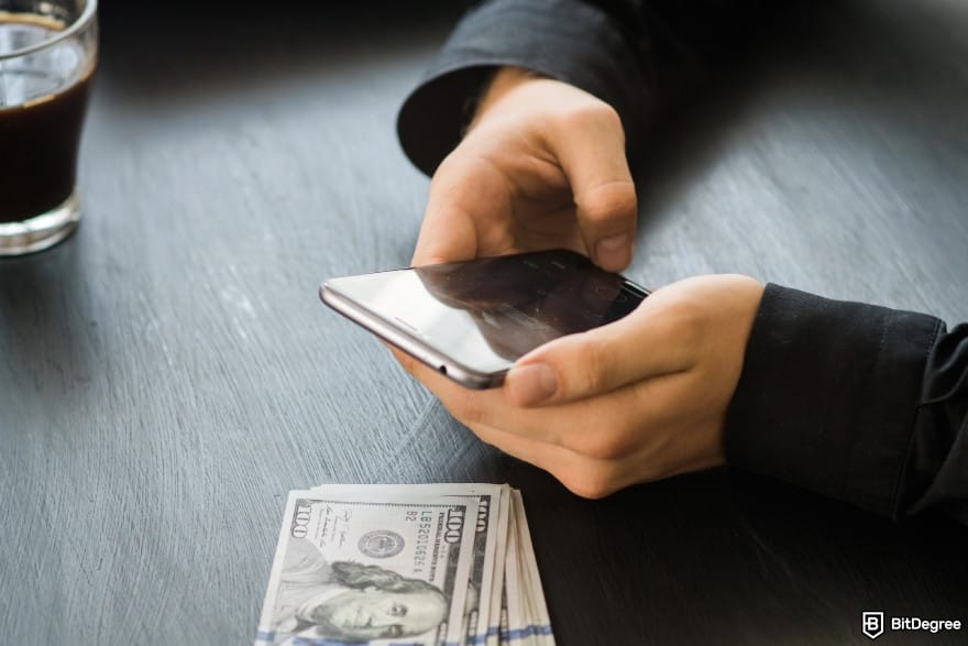 Cheapest way to send money to Philippines: man holding mobile smart phone on black background.