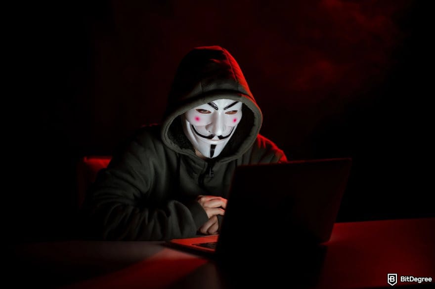 Cluely AI review: a person wearing a black hoodie and a mask sitting in front of a laptop.