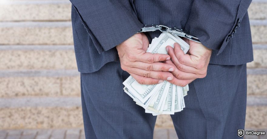 Coinbase fees: a man in a suit holds a stack of money while his hands being cuffed.