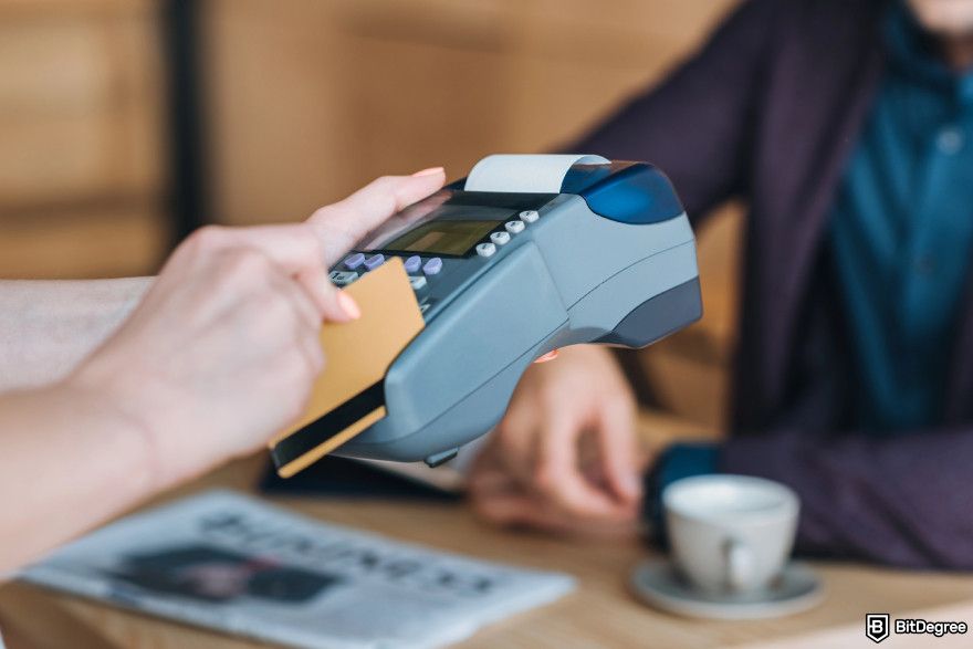 Coinbase fees: a person using a credit card reader while holding a credit card, demonstrating a transaction process.