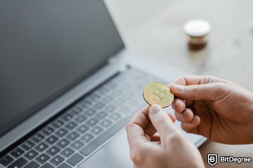 Crypto signals Telegram: Person holding a Bitcoin next to a laptop.