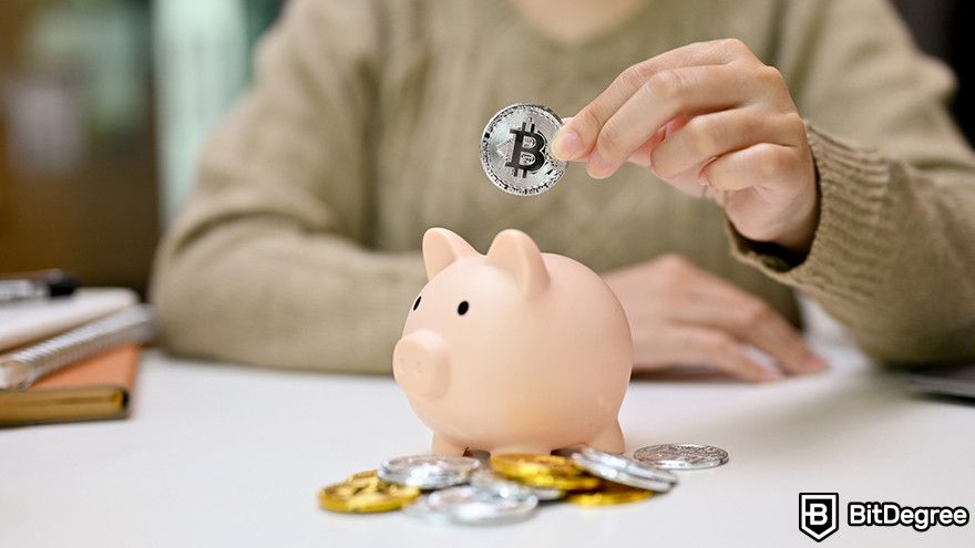 Crypto vs stocks: a person inserting a Bitcoin token into a piggy bank.