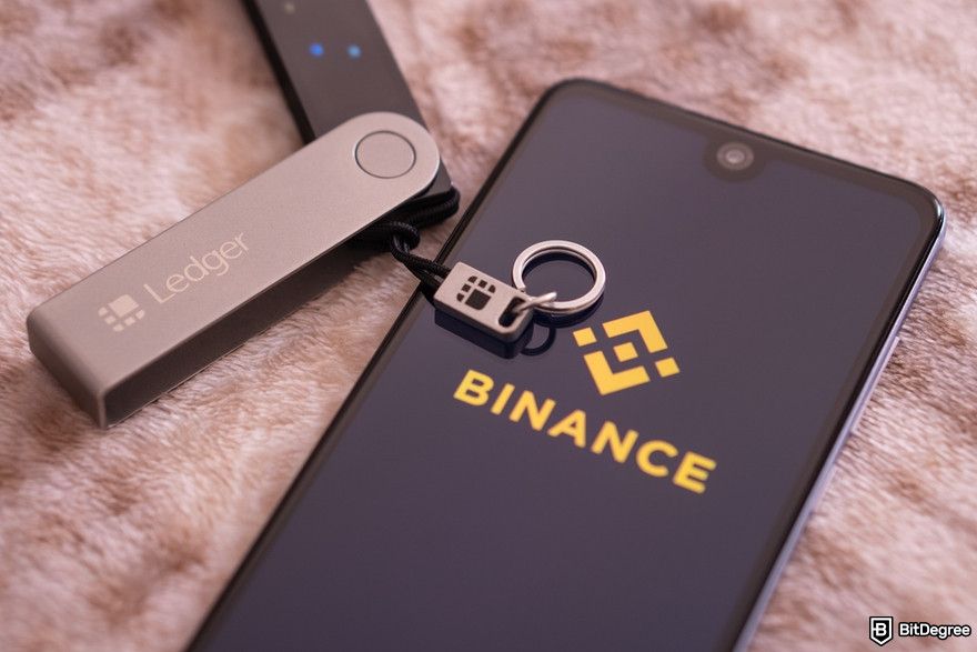 Crypto wallet security: Binance logo on the screen smartphone and Ledger Nano X wallet.