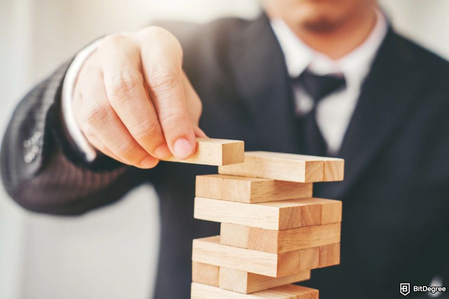 Cryptocurrency jobs: a man stacking jenga to illustrate risk management roles.